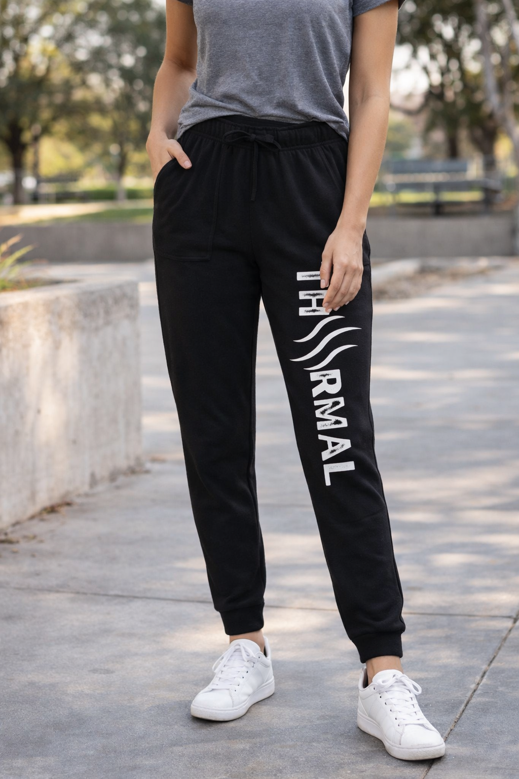 Person wearing black jogger pants with a logo and text, standing outdoors.