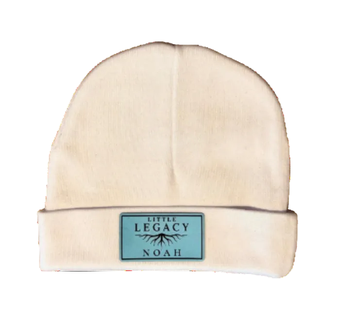 A cream-colored knit beanie hat with a folded cuff, featuring a small rectangular light blue label on the front that reads 'LOVE ALL'. The hat is photographed against a solid white background.