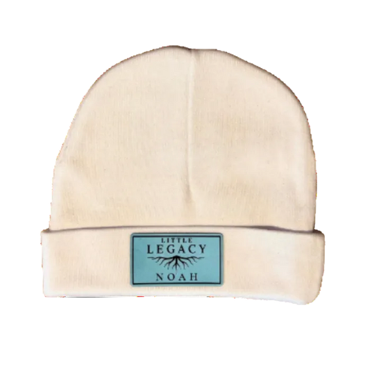 A cream-colored knit beanie hat with a folded cuff, featuring a small rectangular light blue label on the front that reads 'LOVE ALL'. The hat is photographed against a solid white background.